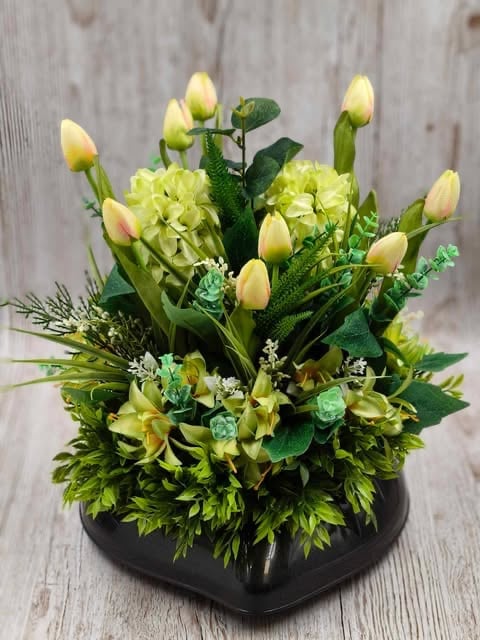 Yellow tulips and green hydrangeas in a black square vase arranged on a wooden surface