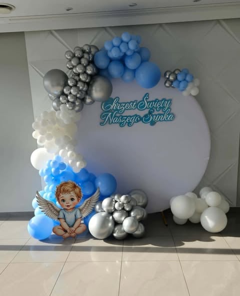 Decorative balloon backdrop with blue, white, and silver spheres, cherub figurine, and Polish christening text sign