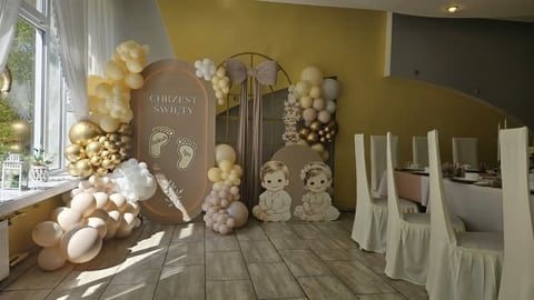 Elegant event space decorated with cream and white balloons, arched backdrop, and white-draped chairs for a religious ceremony.