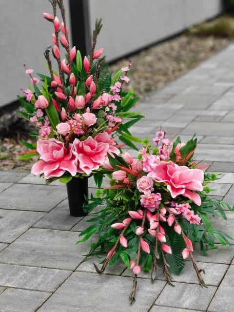 Two pink floral arrangements with carnations and roses on a tiled sidewalk next to a building