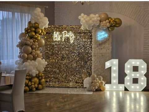 Elegant party backdrop with gold sequin panel, illuminated 18 sign, white cloud balloons, and gold and white balloon clusters