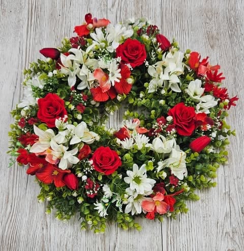 Red and white floral wreath with roses, daisies, and greenery on a weathered gray wooden background