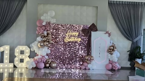 Elegant 18th birthday party setup with rose gold sequin backdrop, pink and white balloons, illuminated number 18, and decorative drapes