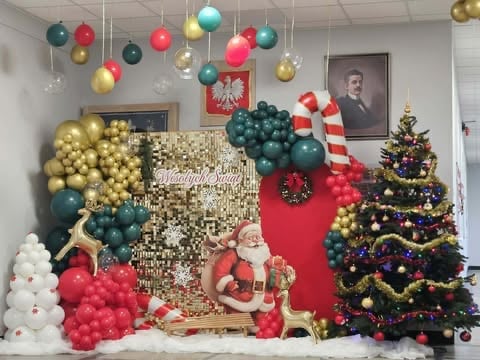 Festive Christmas display featuring gold and red balloons, decorated Christmas tree, ornaments, garland, and holiday decorations