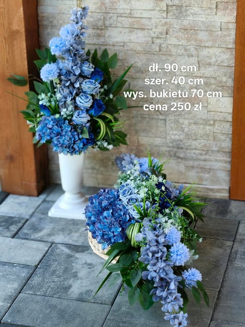 Two blue floral arrangements with hydrangeas and roses displayed against a stone wall, one in a white pedestal vase and one low arrangement on the ground