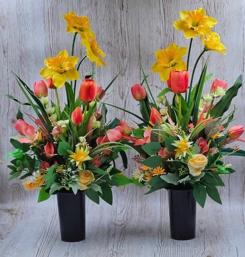 Two black vases with spring flower arrangements featuring yellow daffodils, red and pink tulips, and roses on a gray wooden surface