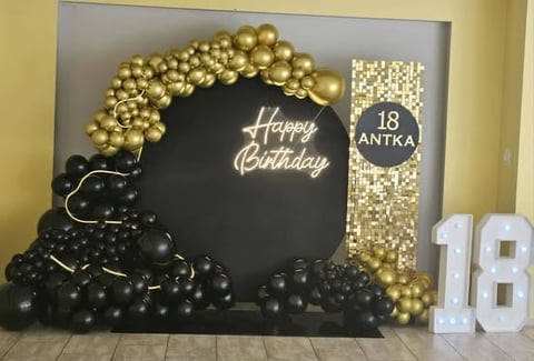 Black and gold 18th birthday party display with Happy Birthday sign, gold balloon arch, and white number decorations
