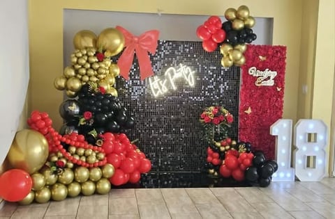 Colorful birthday party backdrop with black sequin panel, red and gold balloons, floral decorations, and Happy Birthday signage.